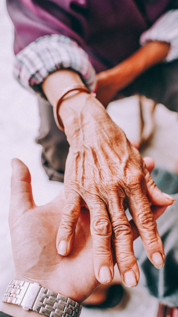 about-us Close-up of a senior's hand being held by a younger hand, symbolizing care and connection.